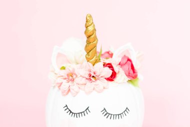 Çiçekli pembe bir arka plan üzerinde beyaz tek boynuzlu at kabak dekore.