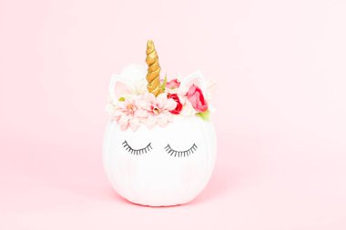 Çiçekli pembe bir arka plan üzerinde beyaz tek boynuzlu at kabak dekore.