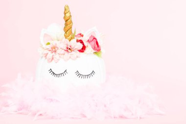 Çiçekli pembe bir arka plan üzerinde beyaz tek boynuzlu at kabak dekore.