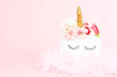 Çiçekli pembe bir arka plan üzerinde beyaz tek boynuzlu at kabak dekore.