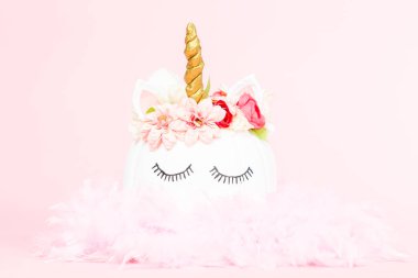 Çiçekli pembe bir arka plan üzerinde beyaz tek boynuzlu at kabak dekore.