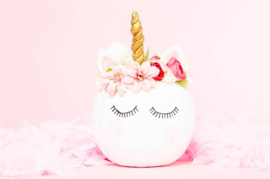 Çiçekli pembe bir arka plan üzerinde beyaz tek boynuzlu at kabak dekore.