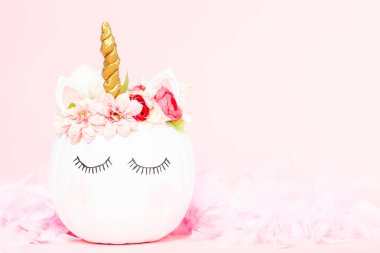 Çiçekli pembe bir arka plan üzerinde beyaz tek boynuzlu at kabak dekore.