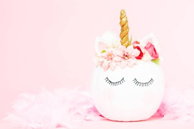 Çiçekli pembe bir arka plan üzerinde beyaz tek boynuzlu at kabak dekore.