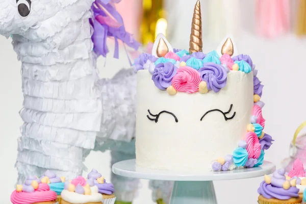 Little girl birthday party table with unicorn cake, cupcakes, and sugaer cookies.