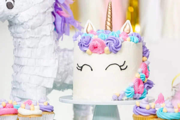 Little girl birthday party table with unicorn cake, cupcakes, and sugaer cookies.