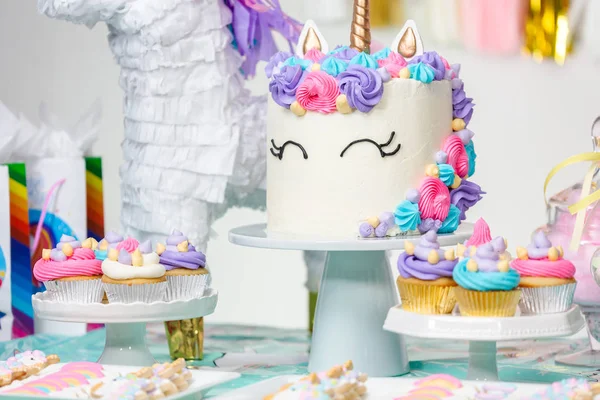 Little girl birthday party table with unicorn cake, cupcakes, and sugaer cookies.