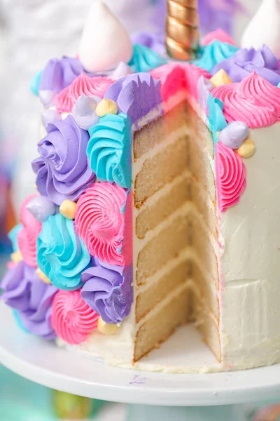 Sliced multilayer unicorn cake on cake stand at the little girl birthday party.