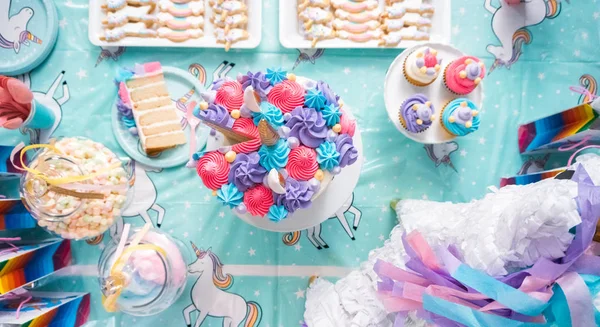 Little girl birthday party table with unicorn cake, cupcakes, and sugaer cookies.