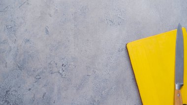 Sarı ağaç kesme tahtası ve bıçağı masanın üzerine.