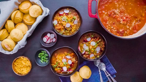 Step by step. Turkey chili garnished with green onions, radishes, and cheddar cheese in black bowls.