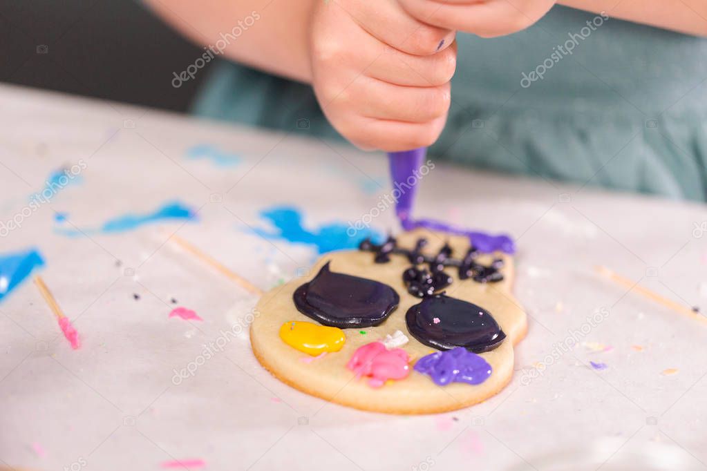 Little girl decorating sugar cookies with royal icing for Dia de los Muertos holiday.