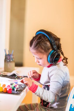 müzik ve sanat proje evde masa üzerinde kulaklık giyen küçük kız.