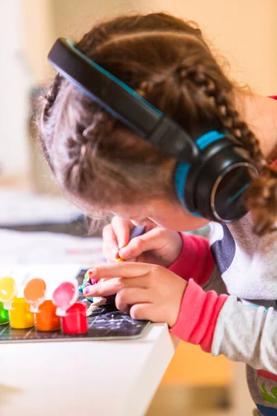 小女孩戴着耳机听音乐和工作在办公桌在家里的艺术项目 — 图库照片