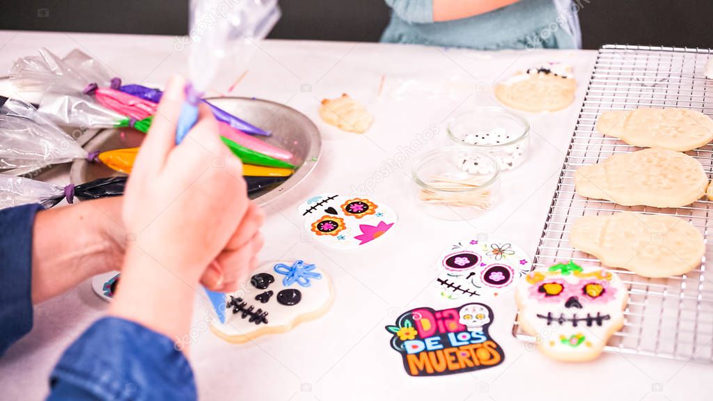 Cropped view of mother and daughter decorating sugar skull cookies with royal icing for Dia de los Muertos holiday.