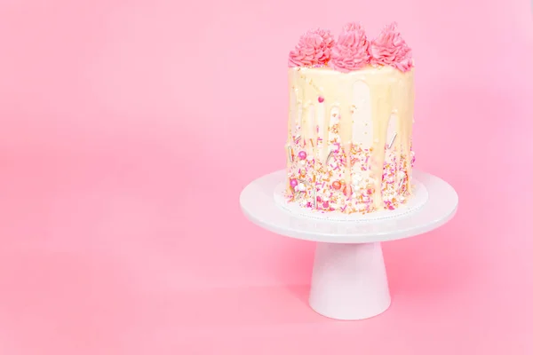 Pink and white buttercream cream cake with pink sprinkles and white chocolate ganache drip.