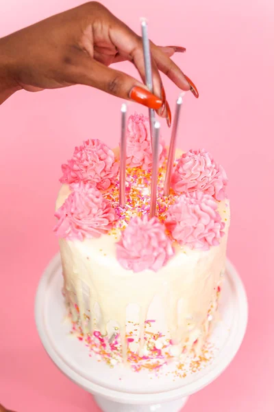 妇女把生日蜡烛粉红色和白色奶油奶油蛋糕粉红色洒和白巧克力甘纳许滴 — 图库照片