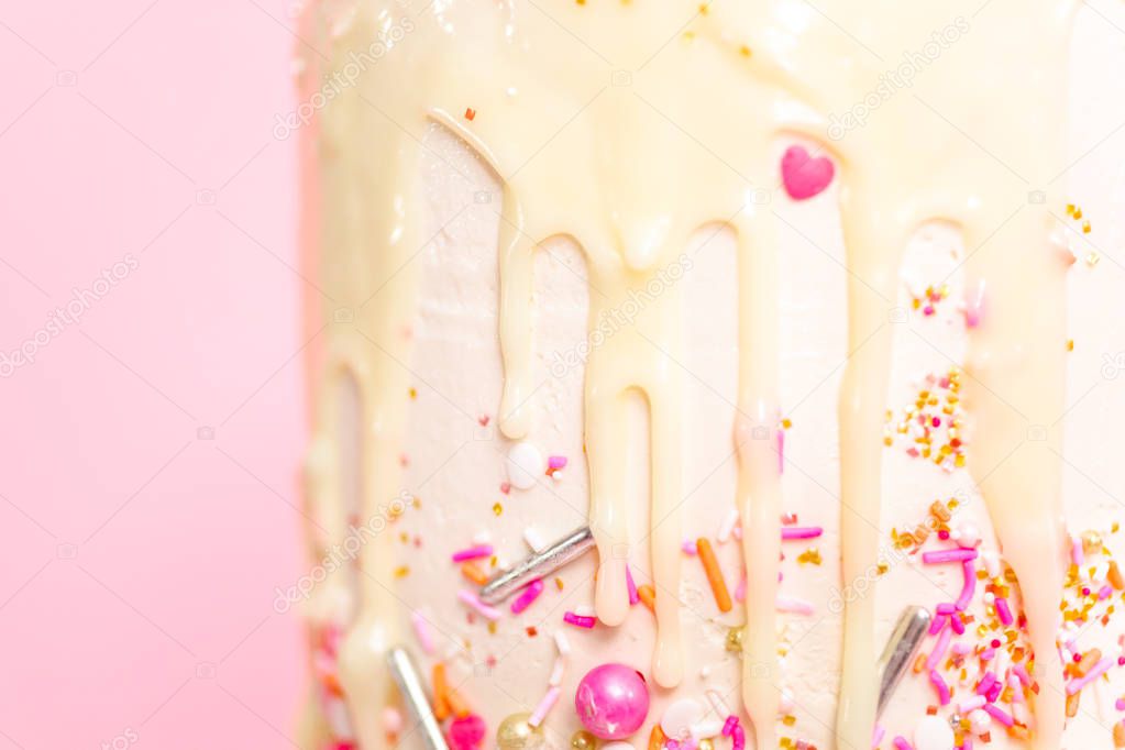Detail of pink and white buttercream cream cake with pink sprinkles and white chocolate ganache drip.