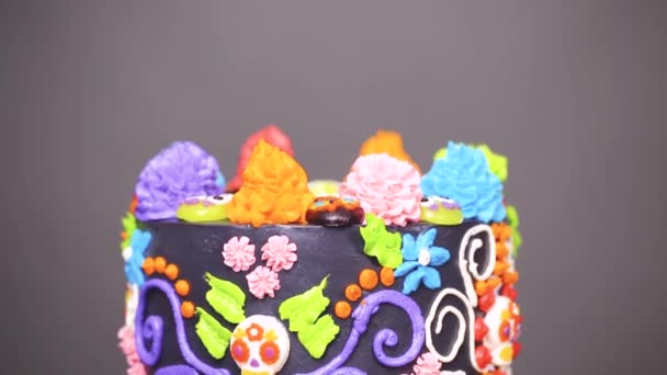 Gourmet dia de los muertos Kuchen dekoriert mit buntem Buttercreme Zuckerguss und Gummy Cupcake Tops auf einem schwarzen Kuchenständer.