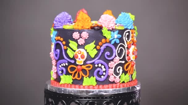 Gourmet dia de los muertos Kuchen dekoriert mit buntem Buttercreme Zuckerguss und Gummy Cupcake Tops auf einem schwarzen Kuchenständer.