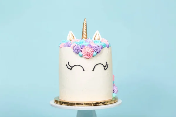 Gourmet unicorn cake with pink and purple buttercream frosting on blue background.