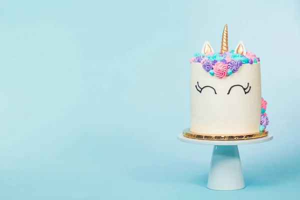 Gourmet unicorn cake with pink and purple buttercream frosting on blue background.