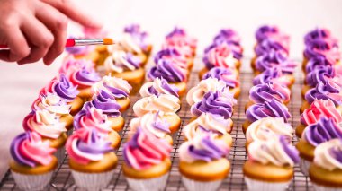 Pembe ve mor buttercream frosting küçük vanilyalı kek üzerinde boru.