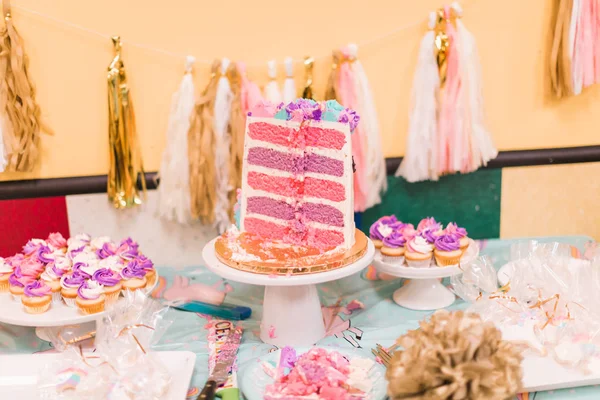 Sliced tall unicorn cake with pink and purple cake layers at little girl\'s birthday party.