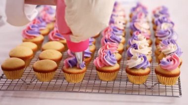 Pembe ve mor buttercream frosting küçük vanilyalı kek üzerinde boru.