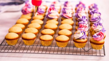 Pembe ve mor buttercream frosting küçük vanilyalı kek üzerinde boru.