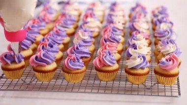 Pembe ve mor buttercream frosting küçük vanilyalı kek üzerinde boru.