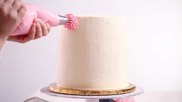 Baker piping pastel color buttercream rosettes on a white cake to make a unicorn cake.