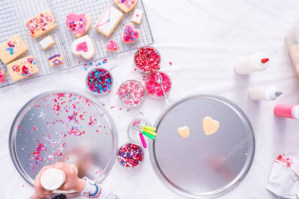 Flat lay. Decorating heart shape sugar cookies with royal icing and pink sprinkles for Valentine's day.