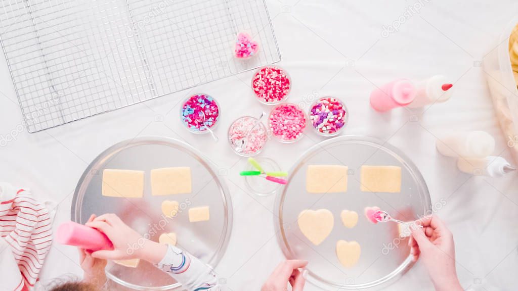 Flat lay. Step by step. Little girl decarting sugar cookies with royal icing and sprinkles for Valentine's Day.
