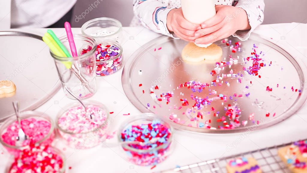 Flat lay. Step by step. Little girl decorating sugar cookies with royal icing and sprinkles for Valentine's Day.