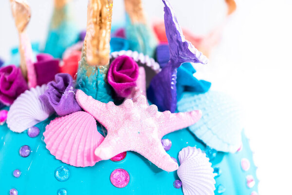 Craft pumpkin decorated in mermaid theme with mermaid tails and seashells for Halloween.