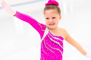 Pembe elbiseli küçük artistik patinajcı kapalı buz pistinde pratik yapıyor..