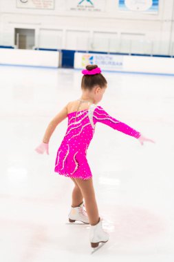 Pembe elbiseli küçük artistik patinajcı kapalı buz pistinde pratik yapıyor..