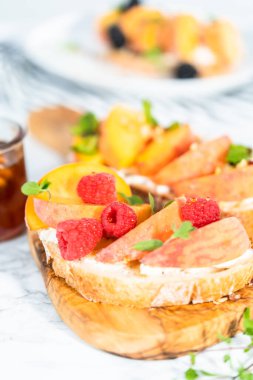 Şeftalili ricotta tostları ceviz, taze nane ve ahududu ile süslenmiş ahşap kesim tahtasında..