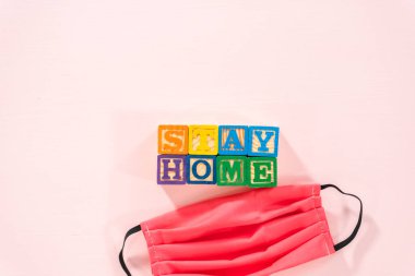 Pembe arka planda ev yapımı yüz maskeleri olan çocukların alfabe bloklarından uzak dur..