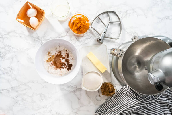 Flat lay. Ingredients to bake pumpkin spice cupcake on a marble countertop.