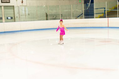 Pembe elbiseli küçük artistik patinajcı kapalı buz pistinde pratik yapıyor..