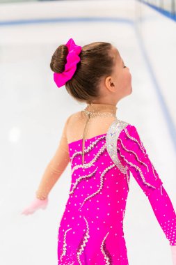 Pembe elbiseli küçük artistik patinajcı kapalı buz pistinde pratik yapıyor..