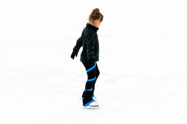 Siyah elbiseli küçük artistik patinajcı, kapalı buz arenasında pratik yapıyor..