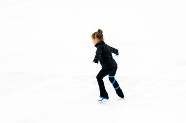Siyah elbiseli küçük artistik patinajcı, kapalı buz arenasında pratik yapıyor..