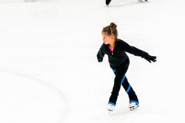 Siyah elbiseli küçük artistik patinajcı, kapalı buz arenasında pratik yapıyor..