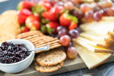 Aperatif olarak sunulan tahtanın üzerinde gurme peyniri, kraker ve meyve var..