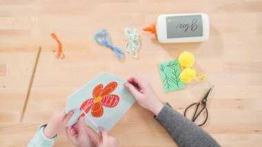 Küçük kız annesiyle el sanatları masasında dikiş dikmeyi öğreniyor..