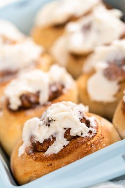 Taze pişmiş tarçınlı rulo, beyaz kremalı, mavi bir tavada..