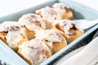 Taze pişmiş tarçınlı rulo, beyaz kremalı, mavi bir tavada..